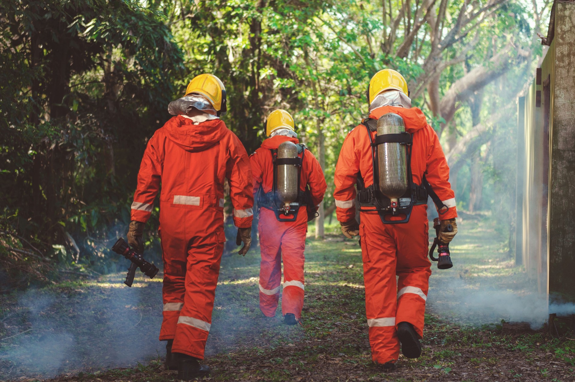 Three firefighters in orange suits walk through a forest